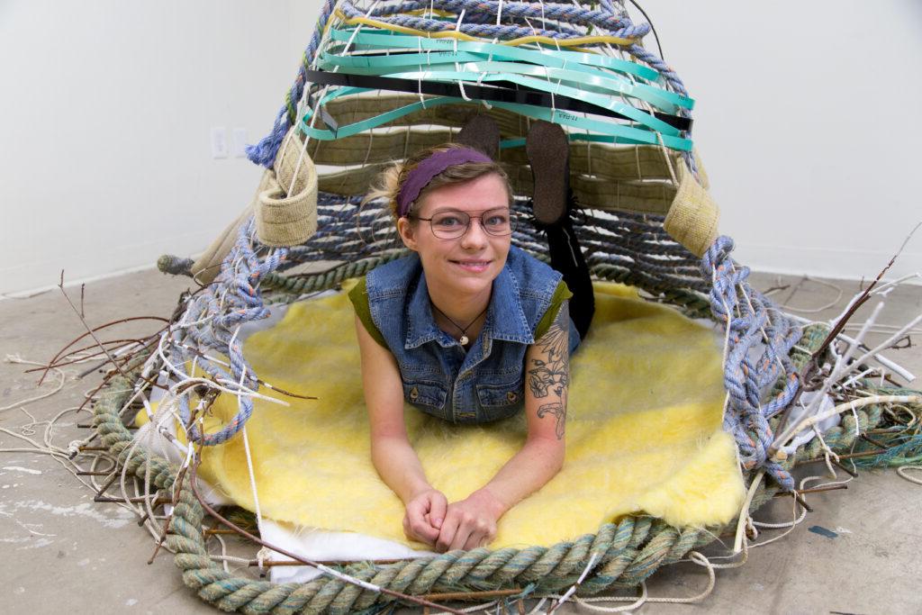 woman laying inside of rope and textile nest sculpture